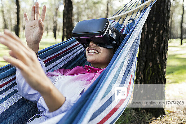 Young woman watching virtual reality simulator gesturing in hammock