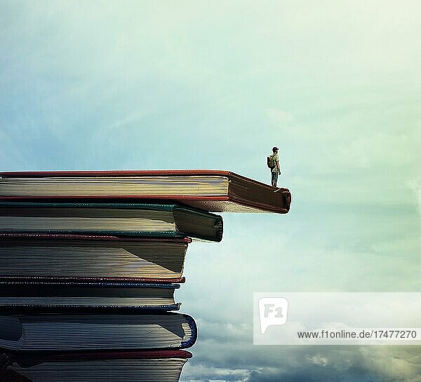 Junge mit einer Tasche auf dem Rücken stehen auf einem Stapel von Büchern Blick weit auf den Horizont. Auf der Suche nach Wissen Konzept
