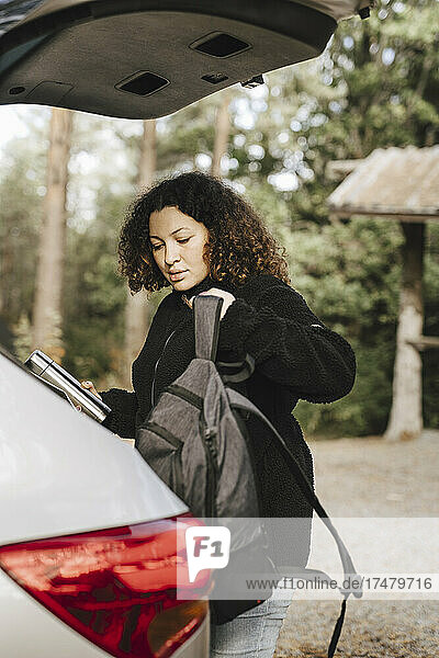 Junge Frau mit Rucksack am Auto im Urlaub