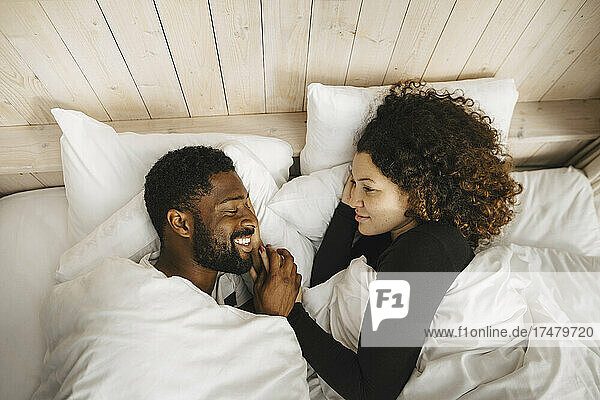Smiling multiracial couple lying on bed in cottage