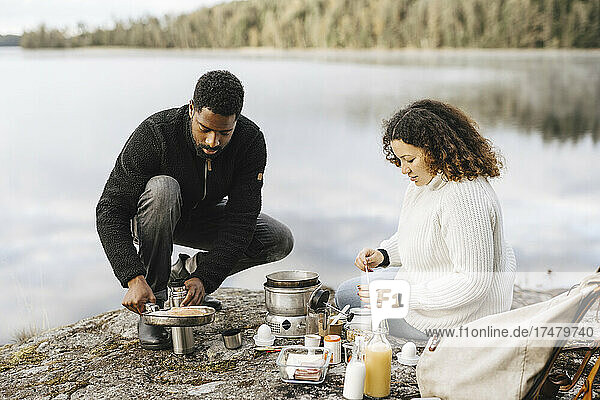 Couple preparing food at lakeshore while camping