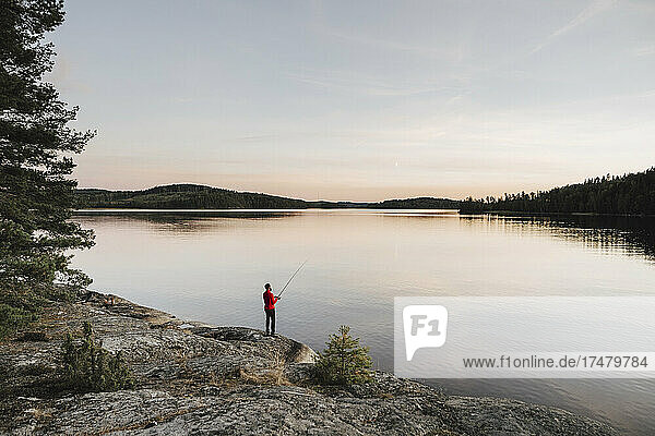 Full length of man fishing at lakeshore during sunset