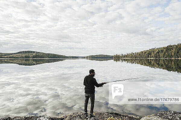 Full length rear view of man fishing in lake with reflection of clouds