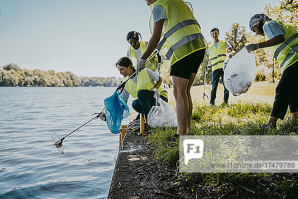 Junge Umweltschützerin und junger Umweltschützer säubern einen See  während sie Plastik aus den Krallen klauben