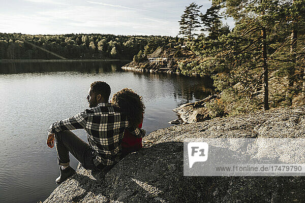 Heterosexual couple spending leisure time while sitting on rock at lake