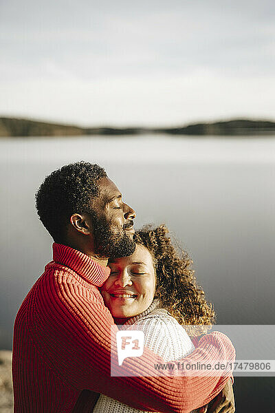 Heterosexuelles Paar umarmt sich am See an einem sonnigen Tag