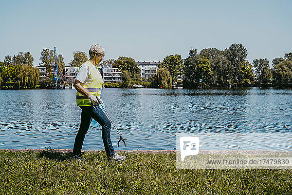 Ältere Klimaaktivistin geht an einem sonnigen Tag mit einer Klaue am See spazieren
