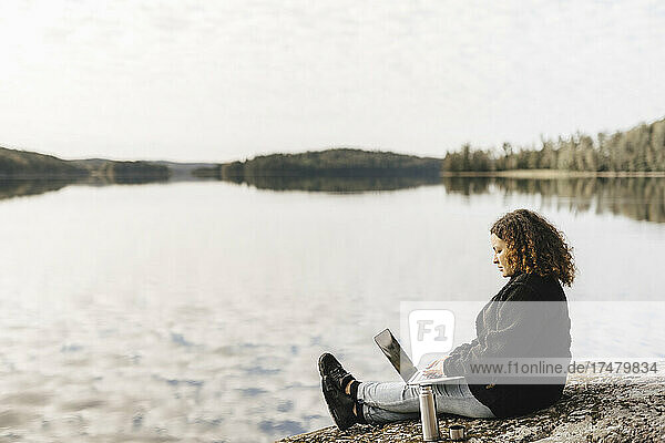 Frau arbeitet am Wochenende ferngesteuert am Seeufer an einem Laptop