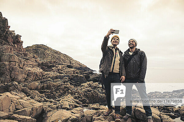 Männliche Freunde machen ein Selfie mit ihrem Smartphone  während sie am Strand stehen