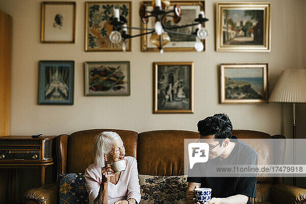 Male caregiver having coffee with elderly woman in living room