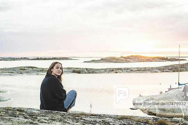 Frau schaut über die Schulter  während sie bei Sonnenuntergang auf einer Insel sitzt