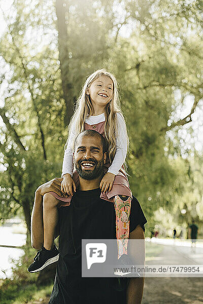 Fröhlicher Vater trägt behinderte Tochter auf den Schultern beim Spaziergang im Park
