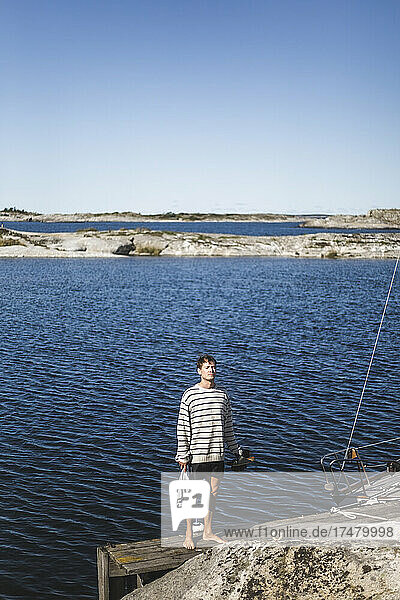Mann steht an einem sonnigen Tag auf einem Steg am Meer
