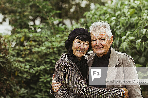 Porträt eines lächelnden älteren Paares  das sich im Urlaub im Park umarmt