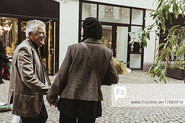 Happy senior man talking with woman while walking on street in city