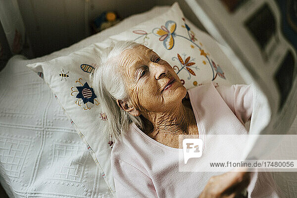 Hoher Blickwinkel auf eine ältere Frau  die auf dem Bett liegend Zeitung liest