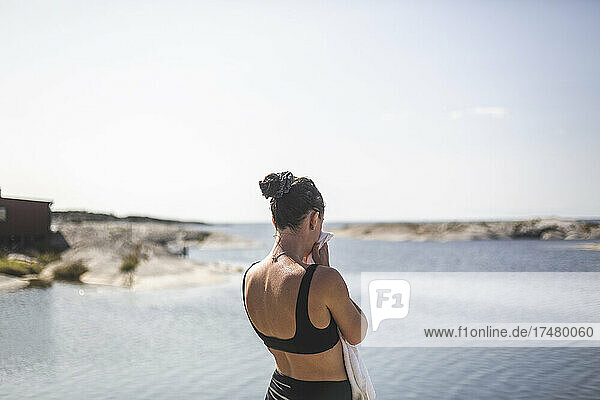 Rückansicht einer Frau mit Handtuch  die an einem sonnigen Tag aufs Meer blickt