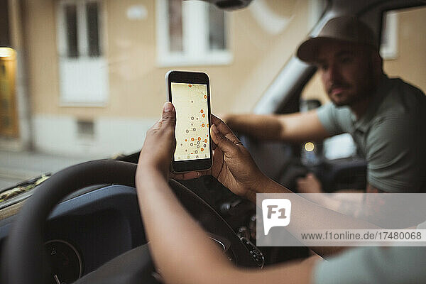 Beschnittenes Bild einer Zustellerin  die das Smartphone eines männlichen Mitarbeiters im Lieferwagen benutzt