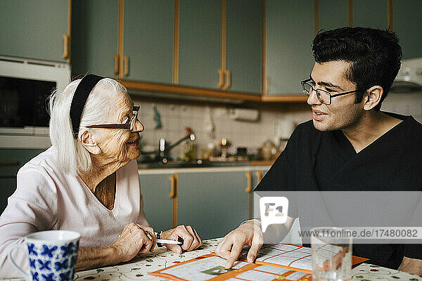 Lächelnde ältere Frau im Gespräch mit Pfleger in der Küche zu Hause