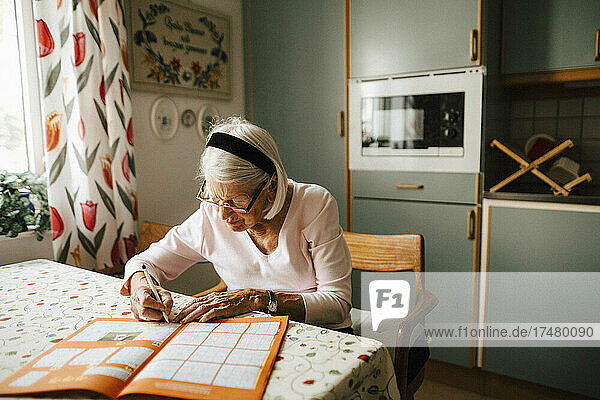 Ältere Frau  die am Esstisch in der Küche ein Sudoku löst