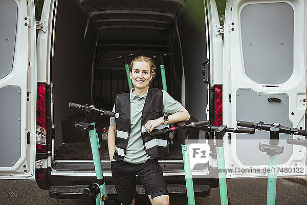 Porträt einer lächelnden Arbeiterin mit Roller vor einem Lieferwagen