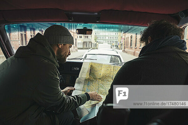 Männliche Freunde  die im Campingwagen sitzend die Landkarte prüfen  während sie einen Ausflug machen