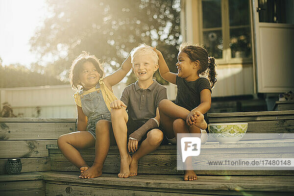 Playful Schwestern mit männlichen Freund sitzen auf Stufen auf der Terrasse während sonnigen Tag