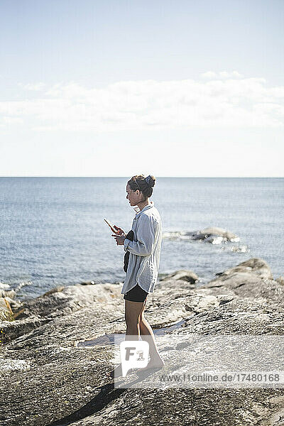 Seitenansicht einer Frau  die im Sommerurlaub auf einem Felsen am Meer spazieren geht