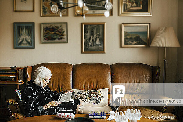Senior woman reading newspaper while sitting on sofa in living room