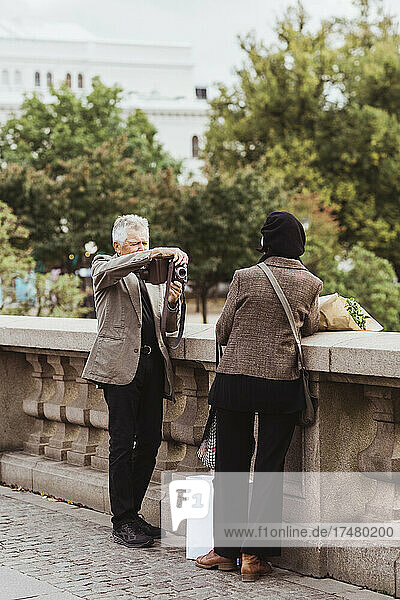 Älterer Mann  der am Wochenende auf einer Brücke eine Frau durch eine Kamera fotografiert