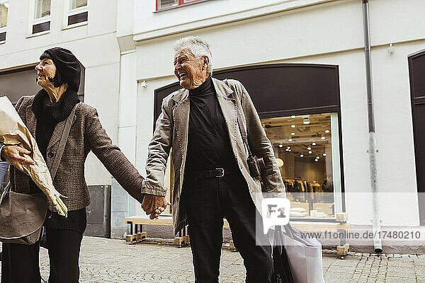Lächelnder älterer Mann hält die Hände einer Frau beim Gehen auf der Straße in der Stadt