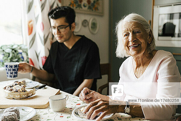 Porträt einer älteren Frau  die mit einem Pfleger in der Küche eines Hauses sitzt
