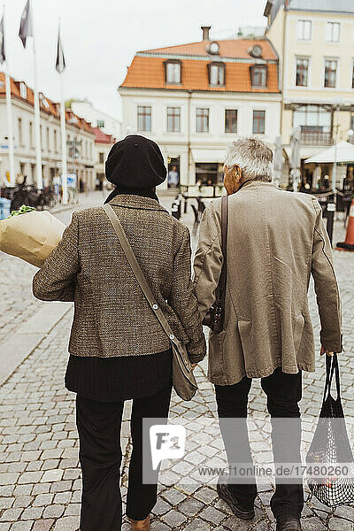 Rear view of elderly couple walking on street in city