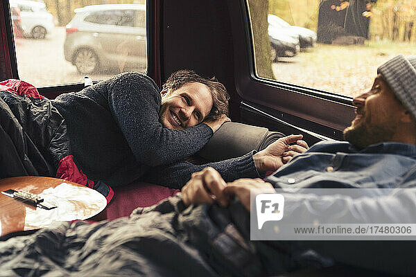 Happy man talking with male friend while lying in motor home during vacation