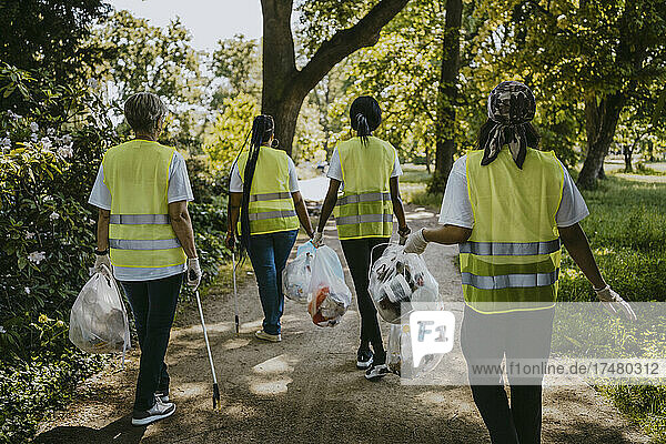 Rückansicht von Umweltschützerinnen  die mit Plastik im Park spazieren gehen