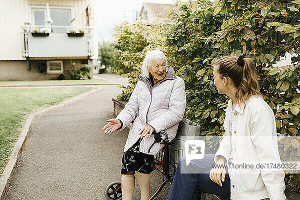 Lächelnde ältere Frau im Gespräch mit einer Krankenschwester im Vorgarten