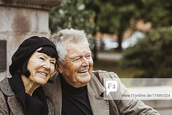 Fröhliches älteres Paar  das im Park sitzt und wegschaut
