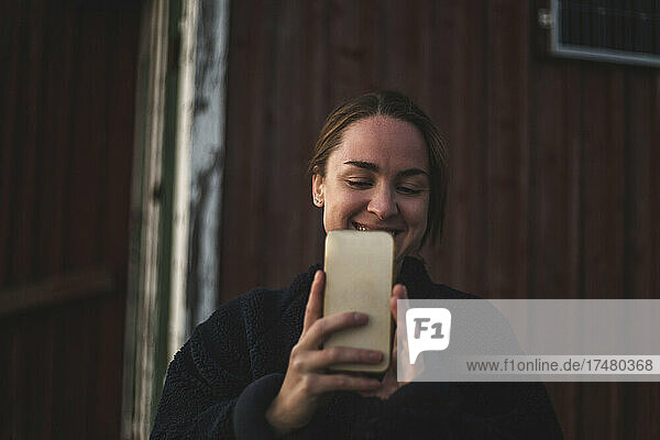 Lächelnde Frau nimmt Selfie durch Smartphone gegen Hütte
