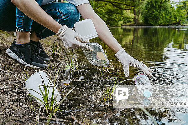 Niedriger Ausschnitt einer freiwilligen Helferin  die einen Teich im Park von Plastikmüll befreit
