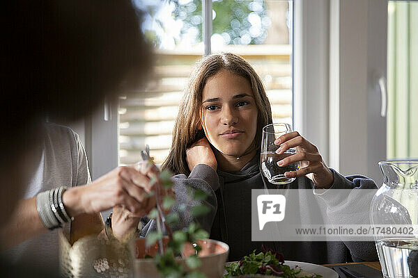 Girl holding drinking glass while having food with mother at home