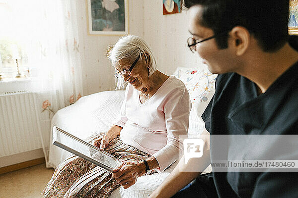 Elderly woman looking in mirror while sitting by male caregiver at bedroom
