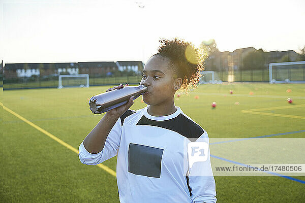UK  Female soccer player (12-13) drinking from bottle in field