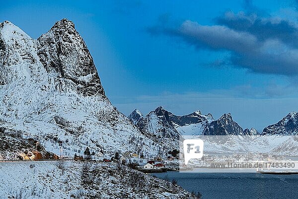 Winterliche skandinavische Landschaft mit erleuchteten roten Häusern  Meer  Berge  Schnee  Hamnøy  Nordland  Lofoten  Norwegen  Europa