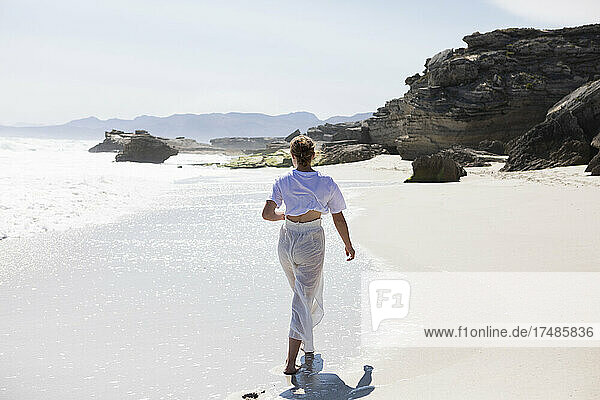 Teenage girl walking on a sandy beach at the water's edge