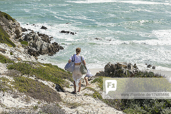Teenage girl and younger brother overlooking a beach and a rocky coastline with waves crashing on shore.