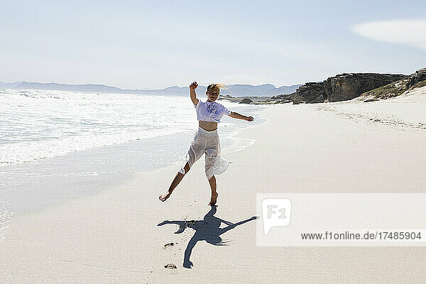 Teenage girl dancing alone on a sandy beach in South Africa by the water's edge