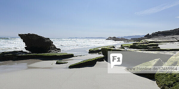 Felsformationen und Klippen mit Blick auf einen Sandstrand  an dem sich die Wellen brechen