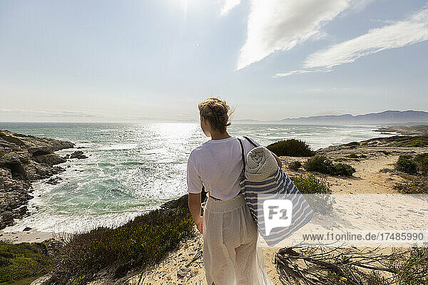 Teenage girl standing on top of a cliff looking over the coastline and inlet.