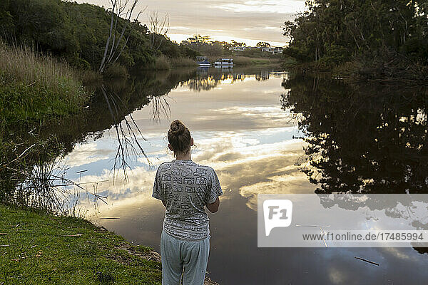 Teenage girl standing by a river at dusk.