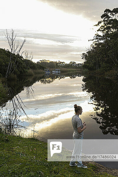 Teenage girl standing by a river at dusk.